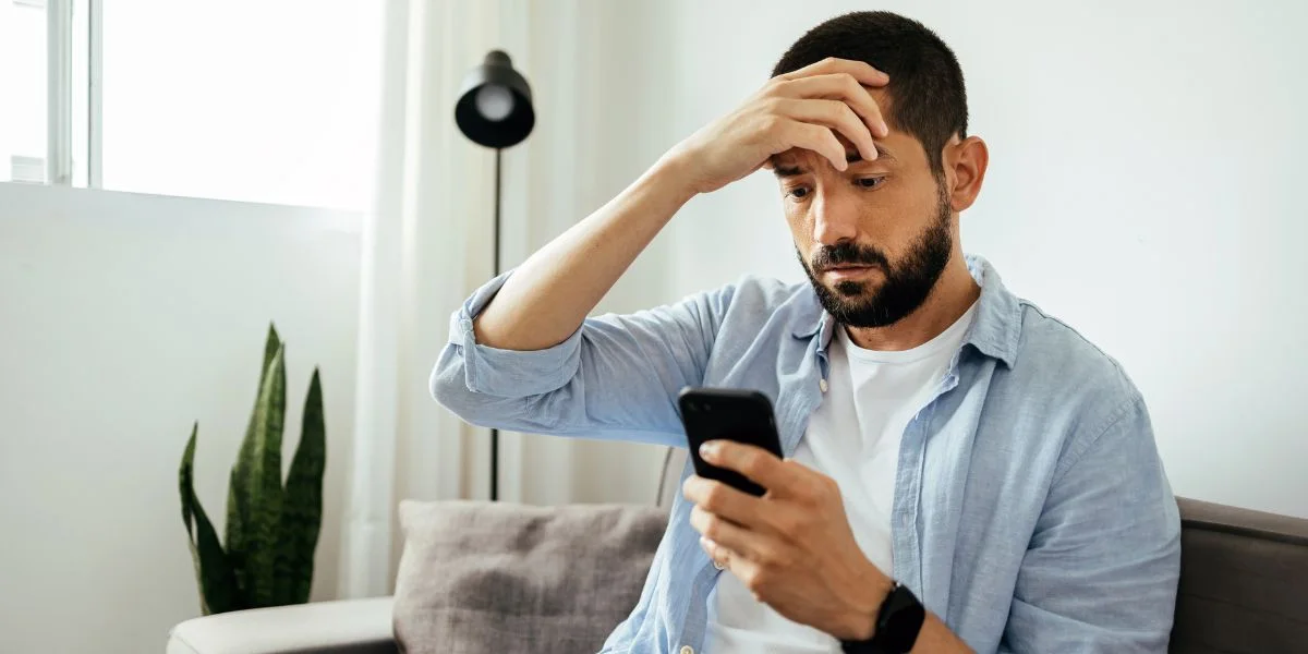 Homem olhando para um celular levando a mão até a cabeça