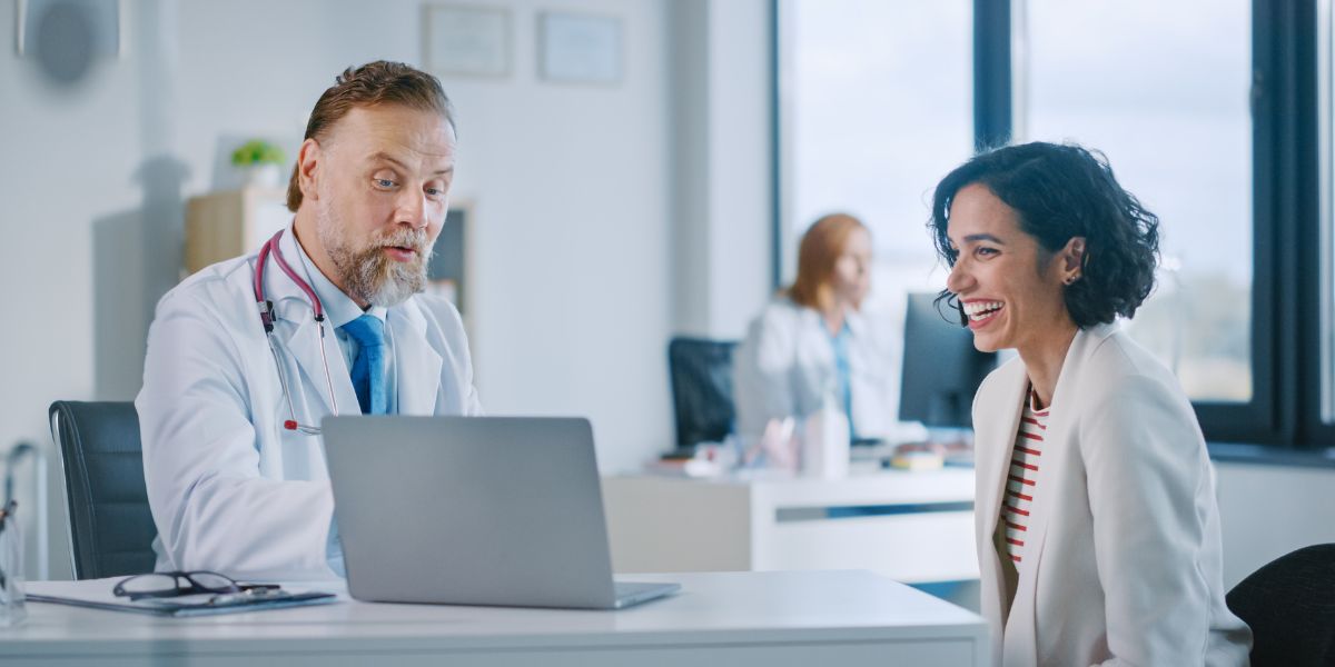 Duas pessoas sentadas atrás de uma mesa olhando a tela de um notebook