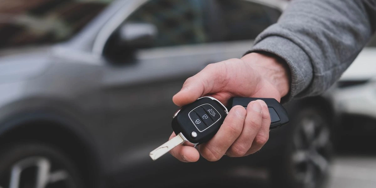 Pessoa segurando a chave de um carro à frente de um veículo