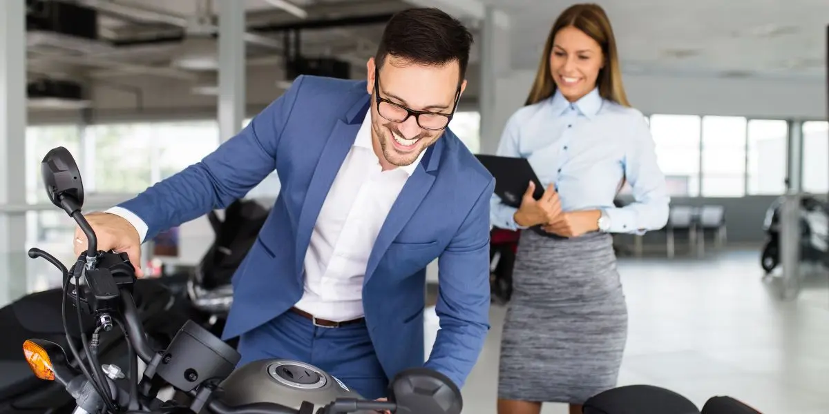 Duas pessoas sorrindo, uma delas sobre uma moto